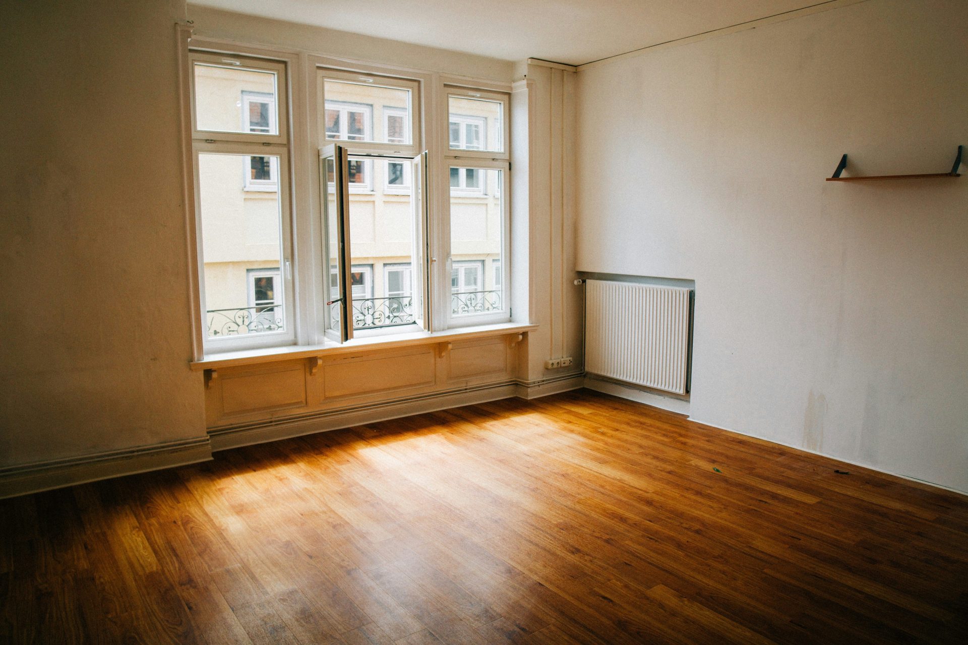 Leerer Raum mit Holzboden und großem Fenster.